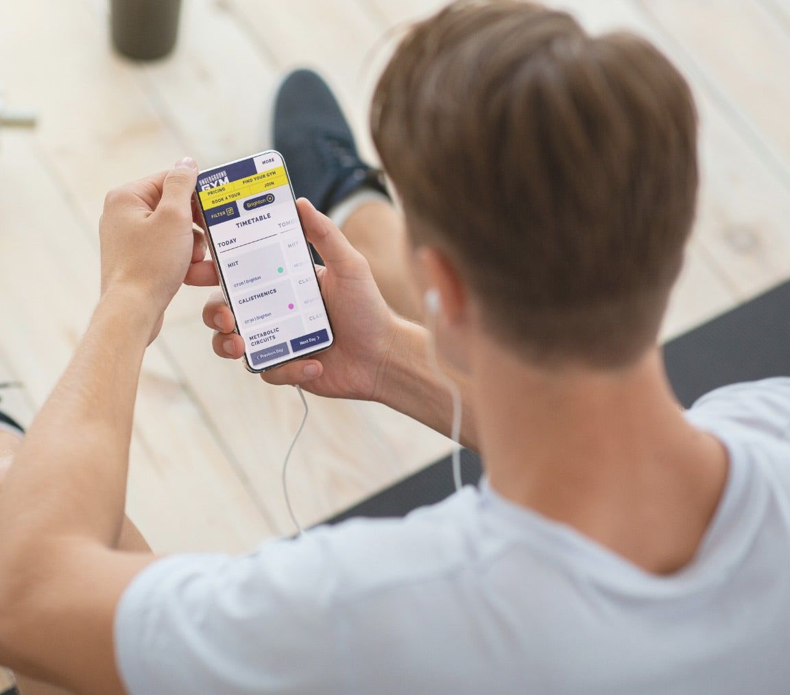 Man working out at home looking at a gym website on his phone